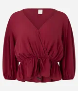 Blusa color vino tinto, con escote cruzado en V, mangas tres cuartos abullonadas con elástico en el puño y peplum ajustado en la cintura con lazo regulable.
