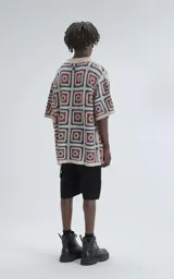 Camisa de manga corta, tejida a crochet con un patrón de cuadrados en colores beige, naranja y turquesa. Presenta cuello tipo polo y cierre frontal con botones.