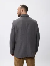 Tapado de paño gris con cierre frontal de botones, cuello clásico y bolsillos laterales. Diseño de corte recto y estructura formal.