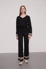 Pantalón negro de tejido de punto con corte palazzo y cintura alta. Presenta dos franjas horizontales color crema en el ruedo.