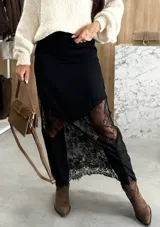 Pollera larga de satén negro con diseño asimétrico y paneles de encaje floral en el ruedo. Presenta una caída fluida y elegante.