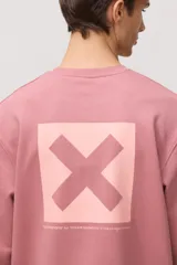 Buzo de cuello redondo en color rosado, con diseño de manga larga y puños acanalados. Presenta un pequeño parche cuadrado con una cruz en el pecho.