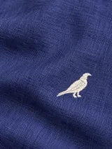 Camisa Club House de lino color blanco, corte slim fit con cuello Hudson, manga larga y detalle de bordado de pájaro azul en el pecho.