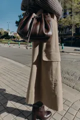 Bolso tipo saca de cuero sintético color marrón oscuro, con diseño fruncido y cierre mediante cordón ajustable. Cuenta con asas de hombro combinadas con cadena metálica y bolsillo interior con cremallera.