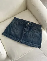 Minifalda de denim azul oscuro con diseño de tiro medio, bolsillos clásicos y detalles deshilachados en el dobladillo inferior.