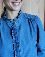 Camisa de jean azul con cuello alto con volados y volados en el frente.