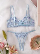 Conjunto de lencería de tul transparente color celeste, con delicado bordado floral en tonos celestes y blancos. Incluye un corpiño con aro y tirantes regulables, y una tanga regulable con tiras finas.