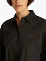 Camisa negra de popelín de mezcla de algodón elástico, corte regular, cuello inglés y puños con botón. Presenta el logo de Tommy Hilfiger bordado en el pecho.