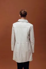 Trench de cuero ovino, de largo midi, con cuello clásico, cierre frontal de botones y diseño de líneas limpias.