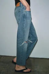 Jeans de tiro medio con corte recto y largo al tobillo. Presentan diseño de cinco bolsillos, cierre frontal con cremallera y botón, y ruedo deshilachado.