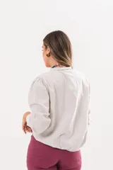 Camisa beige a rayas finas de manga larga, con cuello camisero y cierre frontal oculto.