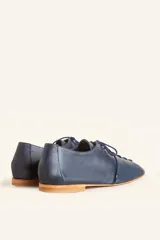Zapato tipo oxford plano de cuero vacuno en color azul marino, con cordones al tono y suela de cuero.