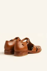 Sandalia cerrada tipo pescador de cuero negro charol, con tira en T y hebilla ajustable en el tobillo. Posee suela y taco bajo de madera.