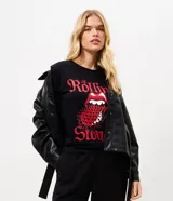 Remera negra de manga corta con cuello redondo y diseño ajustado tipo baby look, confeccionada en algodón con elasticidad. Presenta un estampado frontal con letras rojas y el icónico logotipo de la lengua de The Rolling Stones.