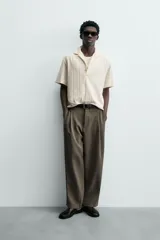 Polo de hombre color crema, de tejido texturado con rayas verticales en relieve, corte relajado, cuello bowling y cierre frontal parcial con botones.