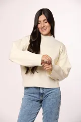 Buzo tejido de punto en color blanco crema, con cuello redondo alto y mangas largas con puños acanalados.