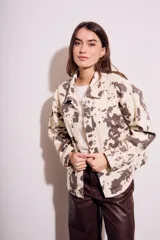 Campera de algodón color crema con estampado de manchas marrones tipo vaca, corte al cuerpo, con cuello clásico, cierre frontal con botones y bolsillos de parche en el pecho.