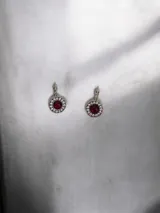 Aros colgantes de acero quirúrgico con diseño circular, piedra central de color rojo y borde engastado con cristales pequeños.