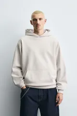 Sudadera tipo hoodie de color blanco hueso, con capucha, manga larga y bolsillo canguro frontal. Presenta un calce relajado y tejido de algodón con interior afelpado.