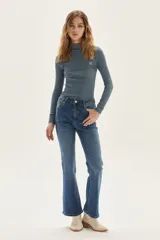 Polera de manga larga con cuello alto, confeccionada en tejido de punto acanalado con diseño de rayas horizontales en color marrón y turquesa. Presenta un bordado pequeño en el pecho y un calce ajustado al cuerpo.