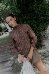 Camisa de corte clásico con estampado de rayas verticales, cuello alto con volados frontales y mangas largas con puños con volados.