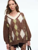 Sweater de tejido de punto con diseño de rombos (argyle) en tonos marrón, verde oliva y crema. Presenta escote en V, mangas largas con puños ajustados y detalles de hilos colgantes decorativos en el frente que le otorgan un aspecto desgastado y moderno.