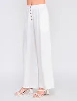Pantalón palazzo color blanco, confeccionado en mezcla de lino y viscosa, de tiro alto con cierre frontal de botones, pinzas en la cintura y piernas anchas.
