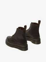 Bota Dr. Martens modelo Sinclair, color marrón oscuro, con plataforma gruesa y suela ranurada. Confeccionada en cuero Crazy Horse, presenta un aspecto desgastado. Incluye cierre frontal de cremallera extraíble, cordones y costura amarilla en el ribete.