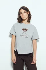 Remera blanca de manga corta con estampa frontal de un personaje con lentes de sol y la frase "Llegué tarde porque no quería venir". Tiene silueta relajada y calce cómodo, con un corte asimétrico en el bajo.