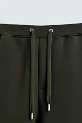 Pantalón de corte wide fit confeccionado en tejido técnico con efecto neopreno. Presenta cintura elástica ajustable con cordón, perneras anchas con costura frontal, bolsillos laterales y bolsillos traseros de plastrón.