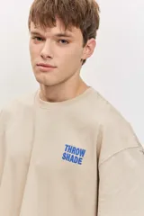 Remera de corte oversize color blanco tiza, de manga corta y cuello redondo, con pequeño estampado gráfico azul en el pecho.