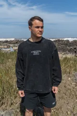 Buzo negro de corte holgado con cuello redondo y mangas largas. Estampado frontal con el texto "Glassy Waves Beach Life".