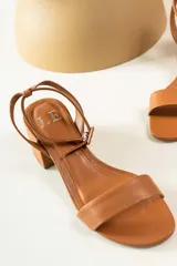 Sandalias de cuero color suela con taco cuadrado bajo y tira ajustable con hebilla en el tobillo.