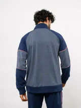 Buzo deportivo de medio cierre marca Umbro del Club Nacional de Football. Presenta un diseño en tonos azul y gris jaspeado, con cuello alto, mangas largas y detalles de costuras en contraste. Incluye el escudo del club y logo de la marca en el pecho.