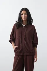 Campera con capucha y cierre frontal, de silueta relajada, hombros caídos y bolsillos laterales. Presenta terminaciones elastizadas en puños y ruedo, con líneas de recorte frontales y cierre metálico con tirador circular.