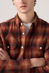 Camisa de manga larga a cuadros en tonos rojo, naranja y negro, con dos bolsillos frontales con solapa y botones blancos.