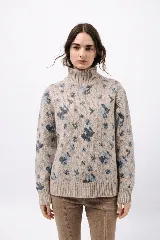 Polera de tejido de punto con cuello alto, diseño holgado y estampado de iconos abstractos en tonos azules sobre base beige. Presenta puños y ruedo acanalados.