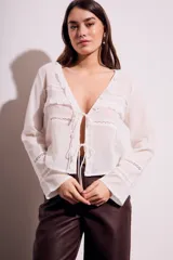 Blusa blanca de algodón con escote en V, mangas largas con detalles de encaje y cierre frontal con lazos.