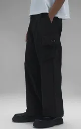 Pantalón estilo técnico de corte oversize, color negro, confeccionado en textil memory. Presenta diseño funcional con cinco bolsillos, incluyendo dos bolsillos cargo laterales de gran tamaño, y cuenta con un cinturón regulable integrado con hebilla de encastre.