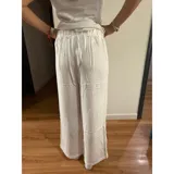 Pantalón palazzo de tiro alto, color blanco, con cierre frontal de doble botón y pinzas en la cintura. Presenta un corte wide leg y bolsillos laterales.