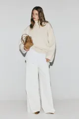Buzo oversized de punto suave, color beige, con cuello alto acanalado y abertura posterior en V. Presenta hombros caídos, costuras decorativas verticales en el frente y terminaciones acanaladas en puños y bajo.