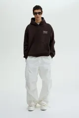 Canguro de mezcla de algodón color marrón oscuro, con capucha cruzada, bolsillo canguro frontal y puños y bajo acanalados. Presenta un estampado pequeño en el pecho con texto y símbolos.