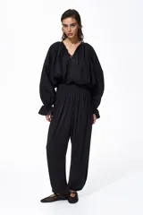 Pantalón negro de tiro alto confeccionado en punto interlock pesado. Cuenta con cintura elástica con pliegues cosidos alrededor, diseño de piernas barrel y puños elásticos ceñidos en los tobillos.