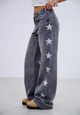 Jean de tiro medio en denim gris lavado, con corte recto y diseño de estrellas bordadas en color blanco a lo largo de los laterales externos de las piernas.