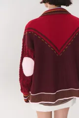 Cardigan de punto con diseño multicolor, cuello tipo polo con rayas, cierre frontal con botones y bolsillos aplicados. Presenta mangas con trama trenzada, coderas en contraste y bordado de la marca en el frente.