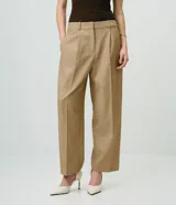 Pantalón de sastrería de crepé color marrón, de corte carrot, con pliegues delanteros, pinzas, bolsillos laterales y cierre frontal.