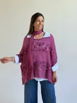 Sweater de punto magenta con diseño holgado, cuello redondo y detalles de encaje floral aplicado en el frente. Incluye una bufanda tipo choker integrada del mismo tejido.