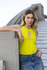 Musculosa amarilla sin mangas de microfibra doble torsión, con calce ajustado al cuerpo y largo hasta la cadera. Presenta detalle de accesorio metálico con sustracción en el escote delantero.