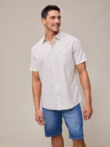 Camisa de manga corta a rayas verticales color blanco y gris, con cuello clásico, cierre frontal con botones, bolsillo en el pecho y logo bordado en el lateral. Corte clásico.