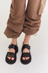 Sandalias negras con diseño de plataforma dentada y tiras ajustables con cierre de velcro. Presentan un acabado texturizado tipo croco.